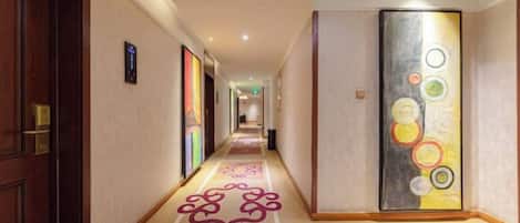 A hotel corridor with a carpeted floor, a door on the left, and a wall with a circular pattern.