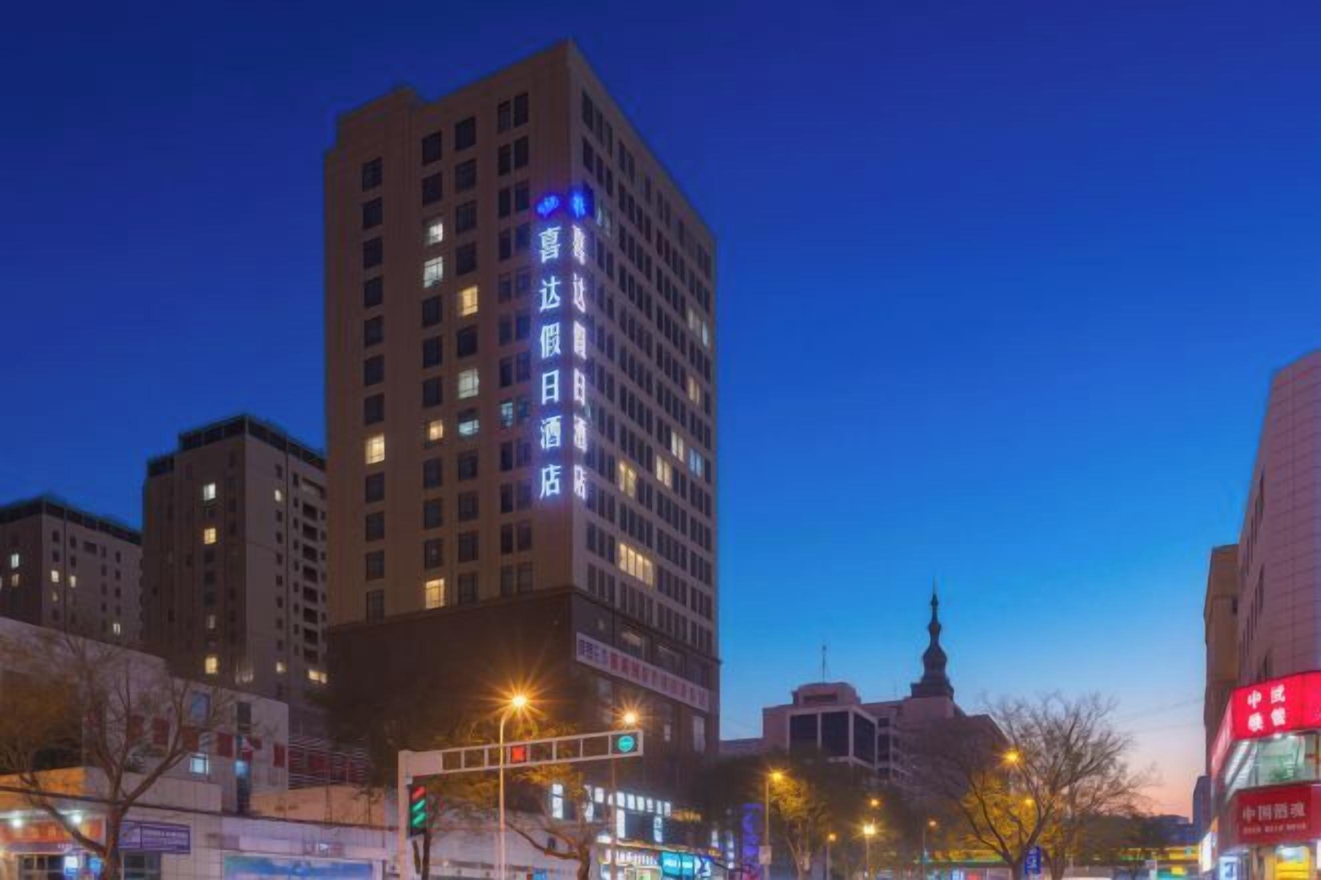 Un immeuble à plusieurs étages avec une enseigne lumineuse, une rue avec des feux de signalisation et d’autres bâtiments en arrière-plan.