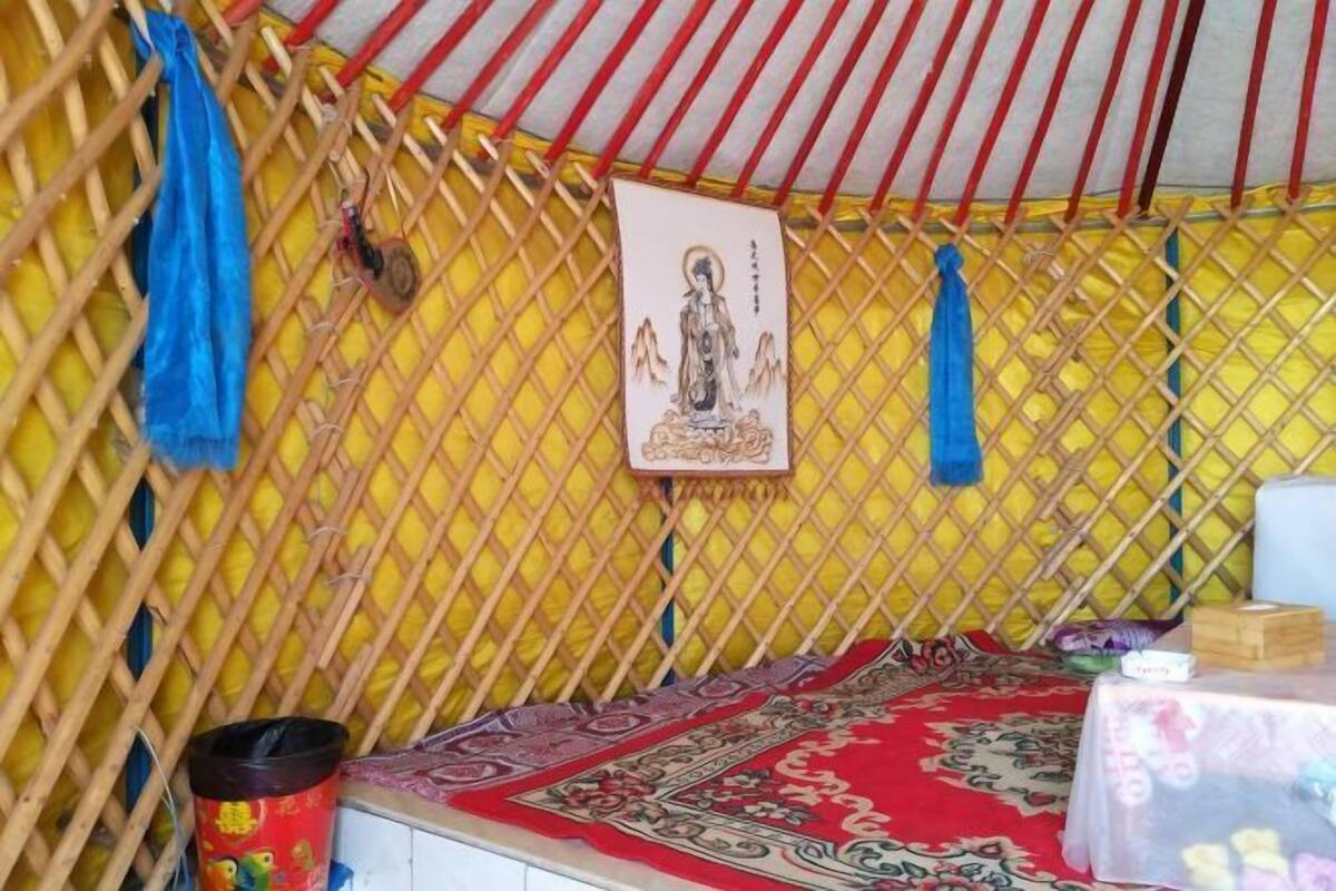 A room with a yellow lattice wall, a red and white striped roof, a patterned rug, and a small table with items on it.