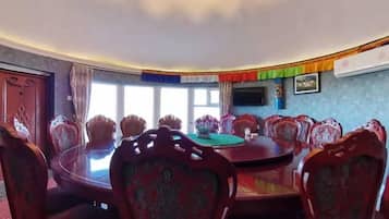 Una mesa de comedor redonda con sillas ornamentadas, un televisor montado en la pared y un ventanal con cortinas.