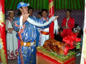 Une personne vêtue d’un costume traditionnel effectue un rituel avec un grand animal rôti.