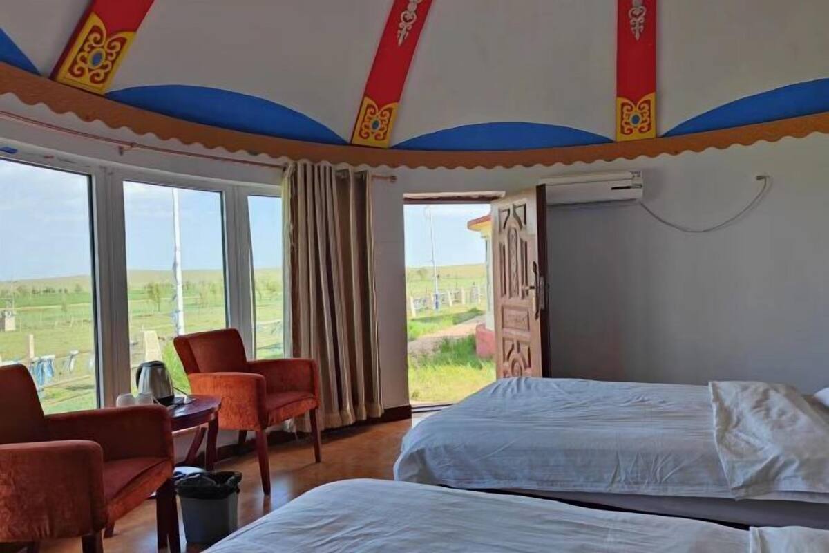 A room with a bed, a chair, a table, and a window with a view of the outdoors.