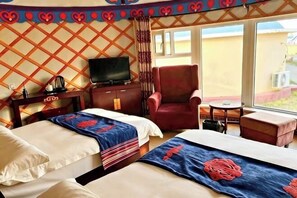 Quarto de hotel com duas camas, uma televisão, uma poltrona vermelha e uma pequena mesa.