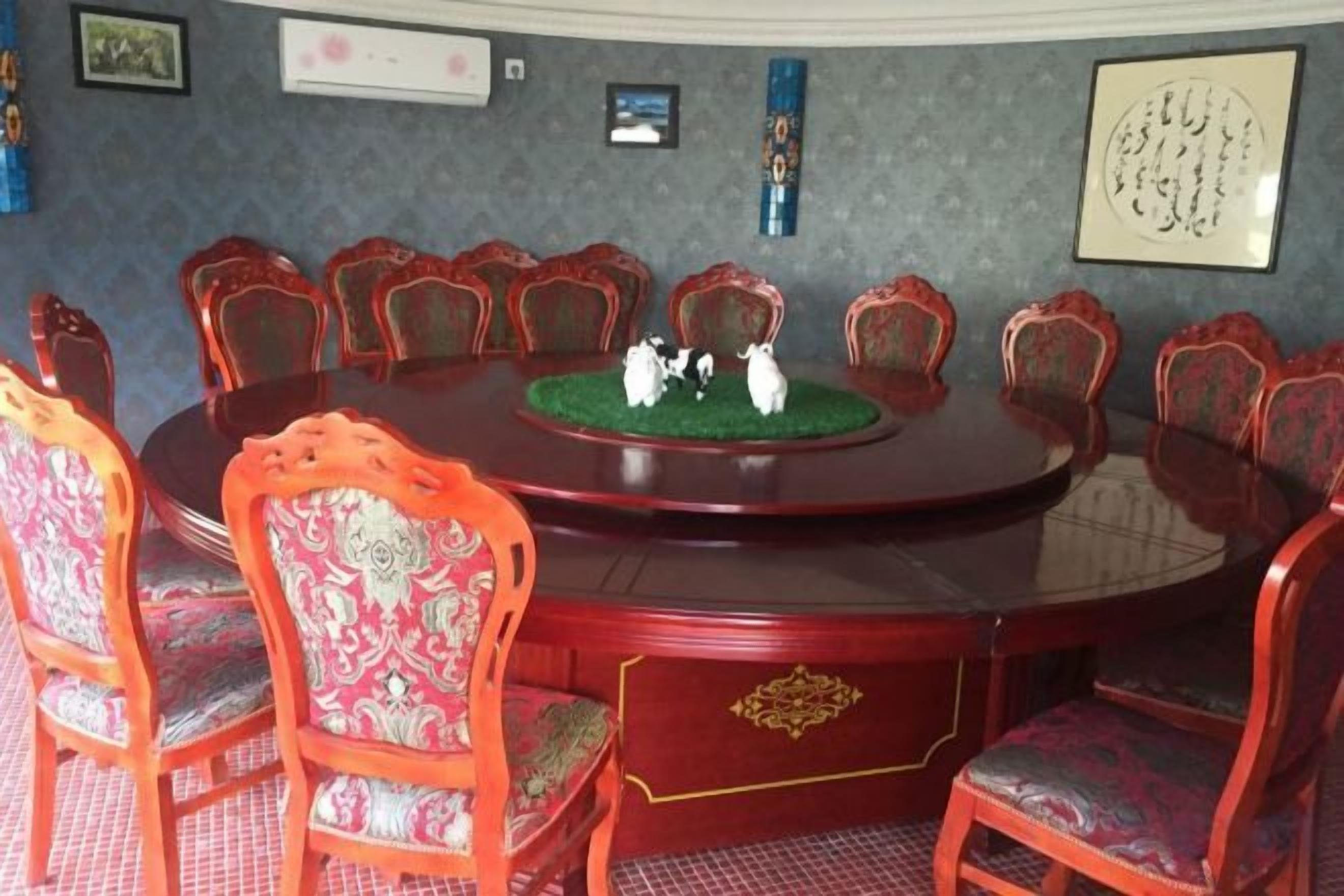 A conference room with a round table, red upholstered chairs, and a green carpet.