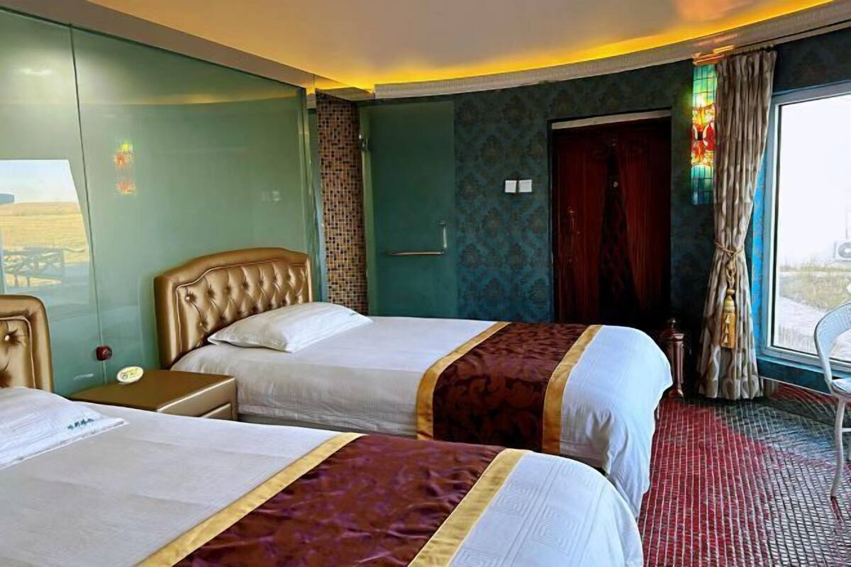 A hotel room with two beds, a nightstand, a desk, a chair, a window with curtains, and a door.