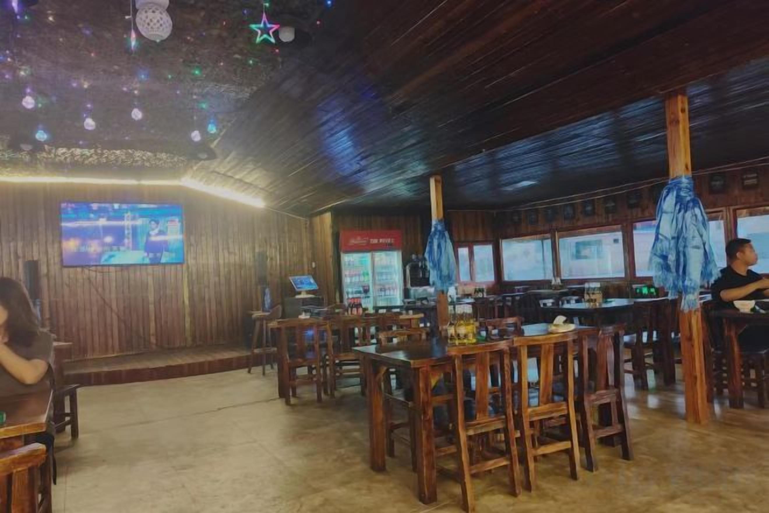 A restaurant with wooden tables and chairs, a television screen, and a bar area.
