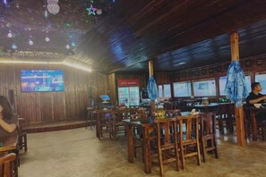 Un restaurant avec des tables et des chaises en bois, un écran de télévision et un coin bar.