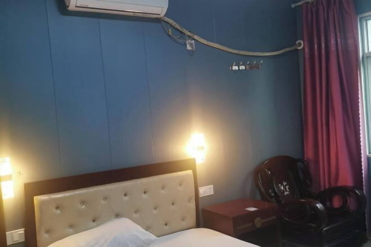 Quarto de hotel com cama, cadeira, mesa de cabeceira e ar condicionado na parede.