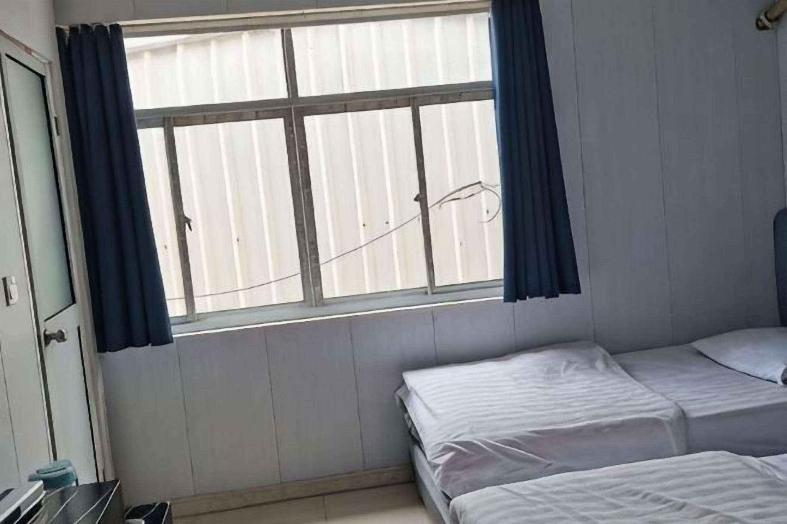 Una habitación con ventana, dos camas, un armario y una mesita.