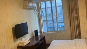 A hotel room with a bed, a TV, a desk, and a window with a view of buildings. - Longyang Inn (Shanghai)