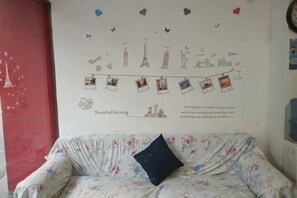 Una habitación con un sofá estampado con motivos florales, una pared adornada con una serie de fotografías y texto, y una puerta roja.