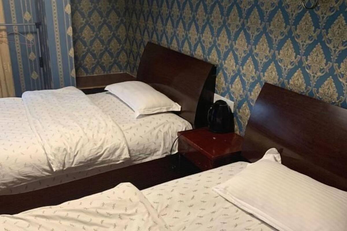 Una habitació d'hotel amb dos llits, un panell de fusta al capçal, una taula petita amb una cafetera i paper pintat amb dibuixos.