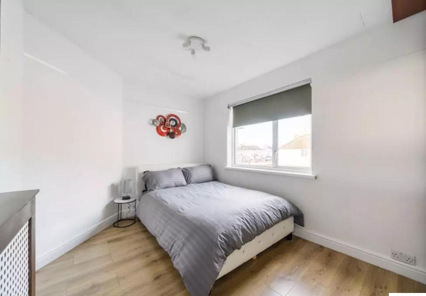 Un dormitorio con cama, ventana, decoración en la pared y una mesita de noche.