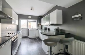 Una cocina moderna con armarios blancos, una encimera negra y dos taburetes de bar.