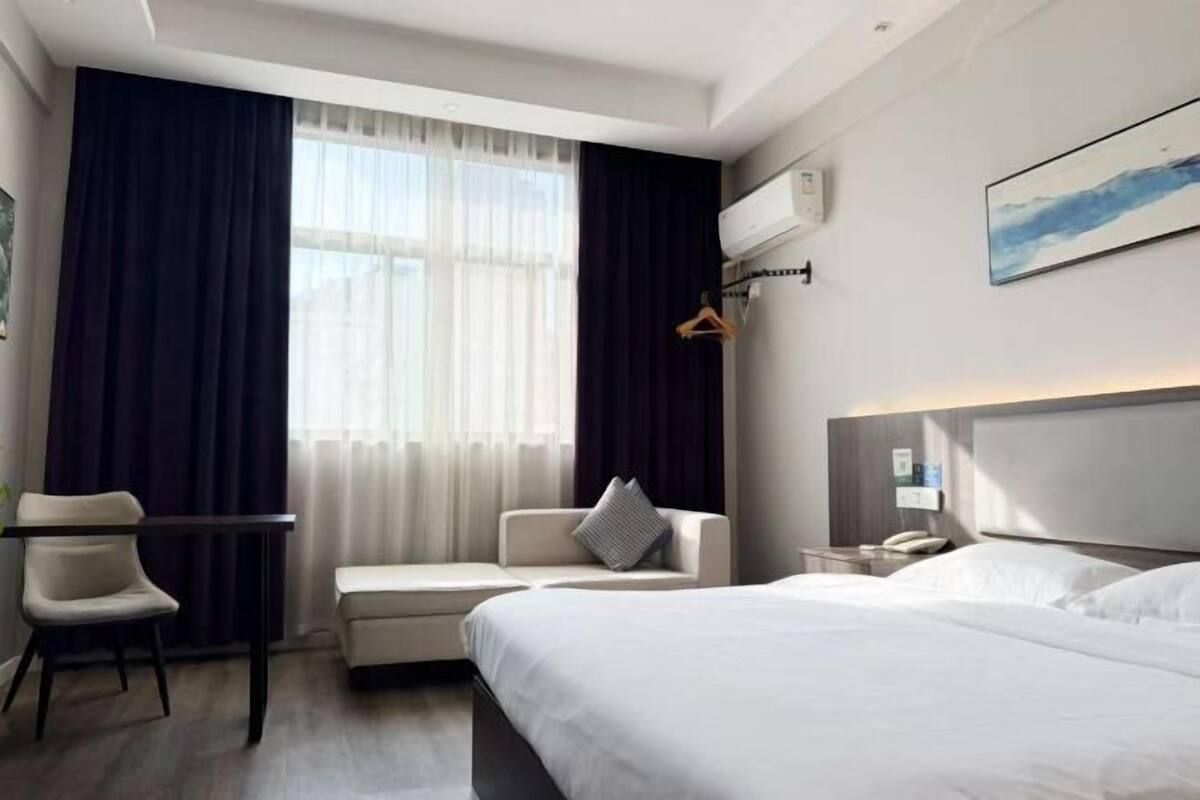 Hotellihuone, jossa on sänky, työpöytä, tuoli, yöpöytä ja ikkuna, jossa on verhot.