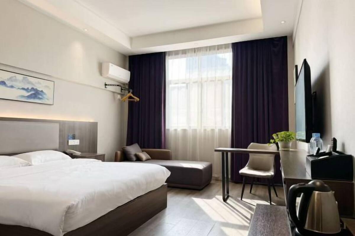Moderni hotellihuone, jossa on suuri sänky, työpöytä, sohva ja suuri ikkuna, jossa on verhot.