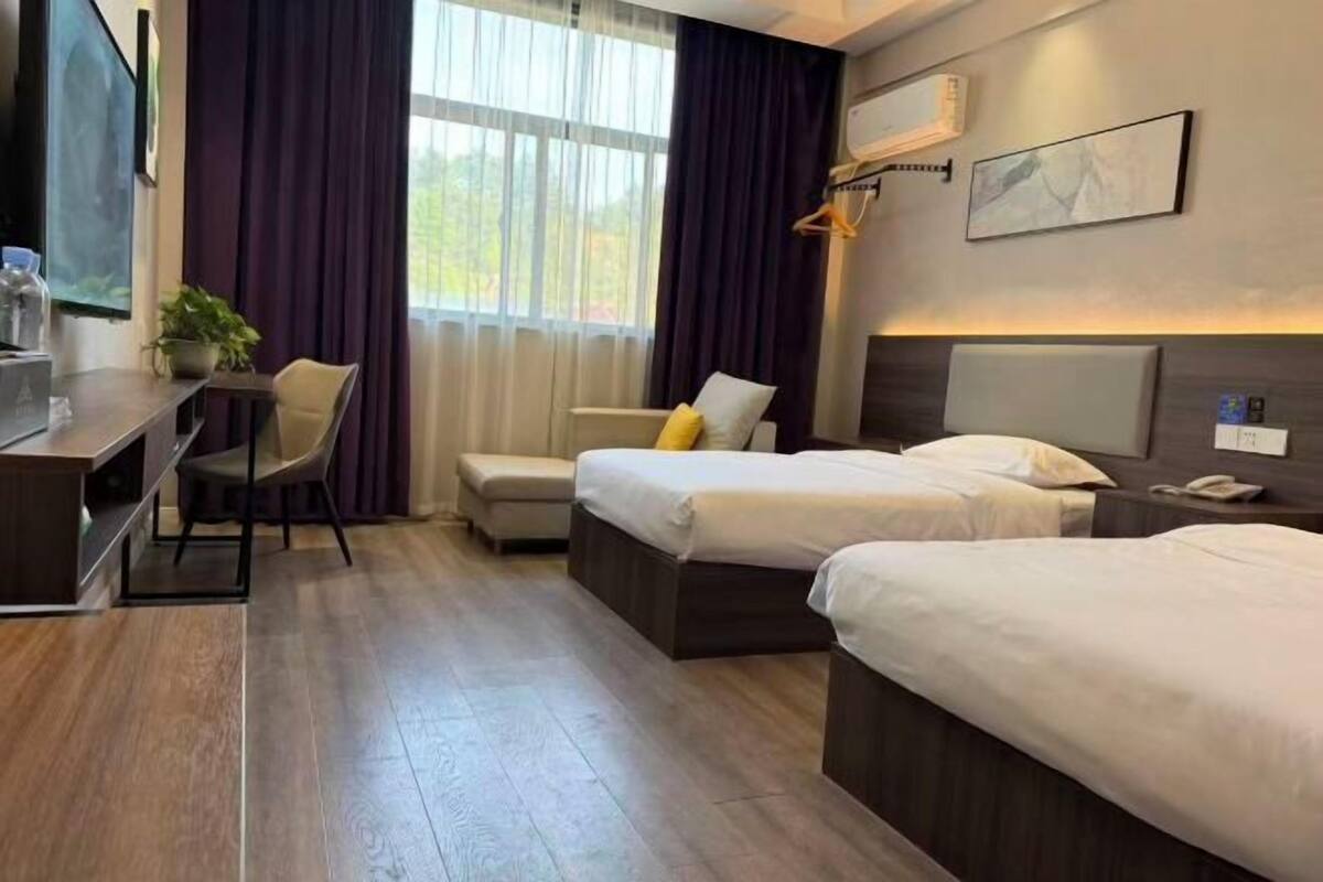 Hotellihuone, jossa on kaksi sänkyä, työpöytä, tuoli, pieni pöytä ja ruukkukasvi.