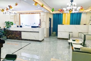 Zona de recepció d'hotel amb mostrador de marbre, espai d'estar i una finestra gran amb cortines.