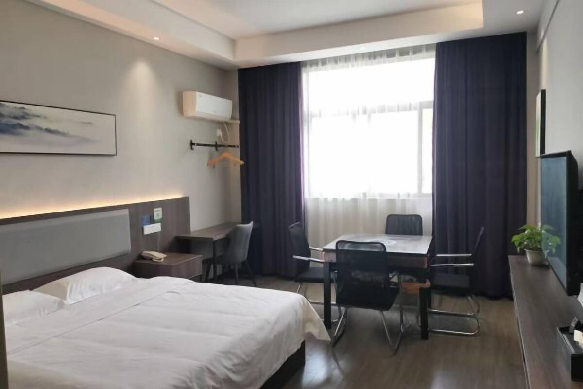 Hotellihuone, jossa on sänky, työpöytä, tuoli, televisio ja ikkuna, jossa on verhot.