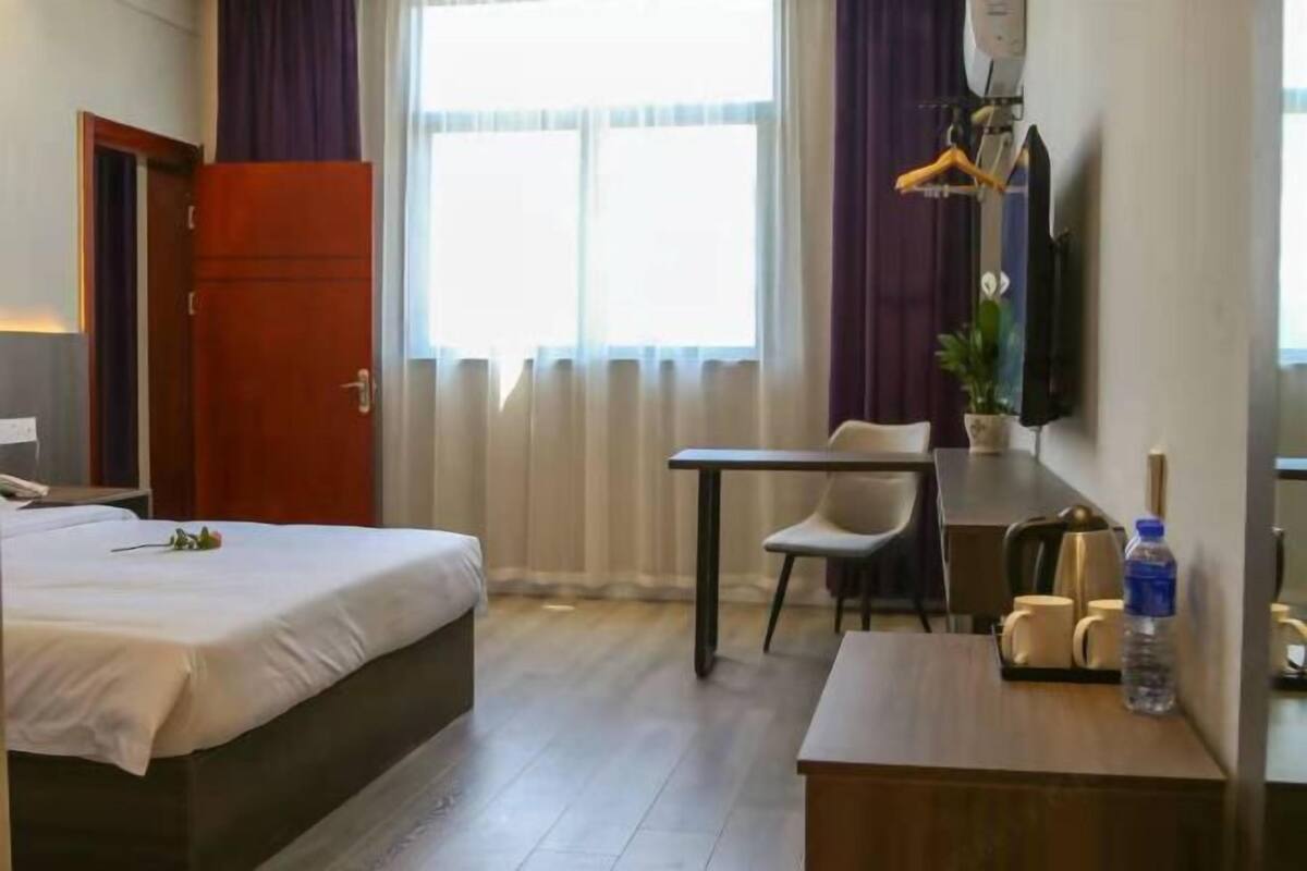 Hotellihuone, jossa on sänky, työpöytä, tuoli, televisio ja ikkuna, jossa on verhot.