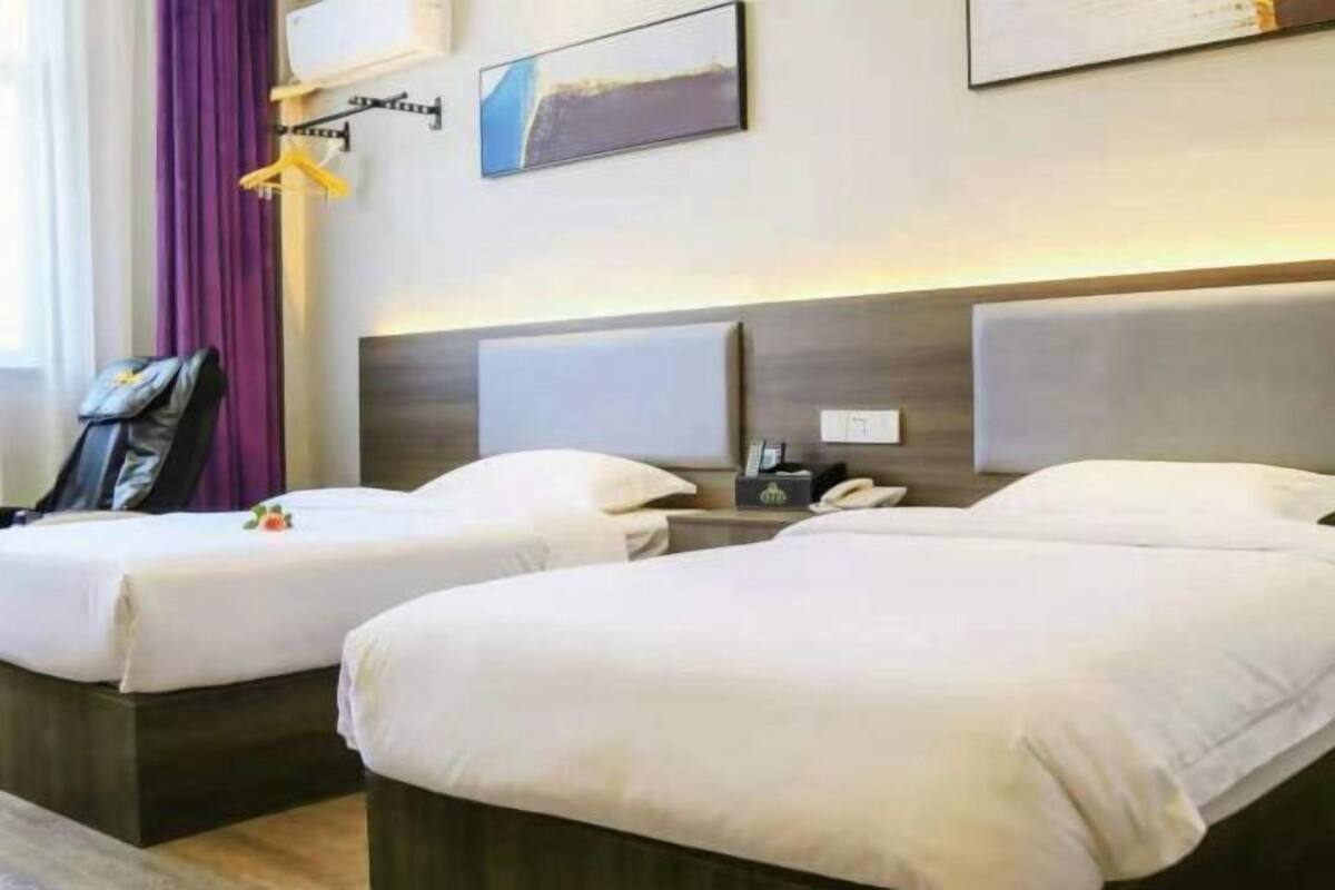Hotellihuone, jossa on kaksi sänkyä, yöpöytä, jossa on puhelin, naulakko ja taulu seinällä.