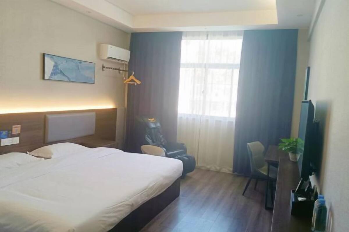 Hotellihuone, jossa on sänky, työpöytä, tuoli, televisio ja ikkuna, jossa on verhot.