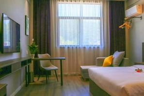 Habitació d'hotel amb llit, escriptori, cadira, televisió i finestra amb cortines.