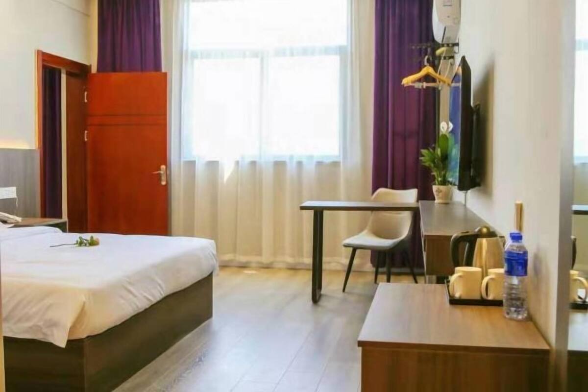 Hotellihuone, jossa on sänky, työpöytä, tuoli, televisio ja ikkuna, jossa on verhot.