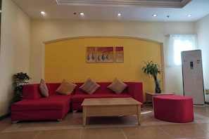 A living room with a red sofa set, a wooden coffee table, and a red ottoman. There is a wall-mounted artwork above the sofa and a potted plant to the left. - Home Inn (Beijing apple garden subway station store) (Beijing)