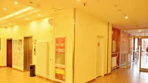 A hotel corridor with a tiled floor, a trash bin, and a glass elevator door. - Home Inn (Beijing apple garden subway station store) (Beijing)