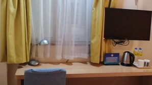 A hotel room with a desk, a chair, a TV mounted on the wall, a window with sheer curtains, and a small table with a kettle, cups, and a bottle of water. - Home Inn (Beijing apple garden subway station store) (Beijing)