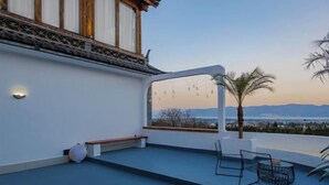 A rooftop terrace with a view of the cityscape, a palm tree, and a seating area with a table and chairs. - When we first meet (Dali City)