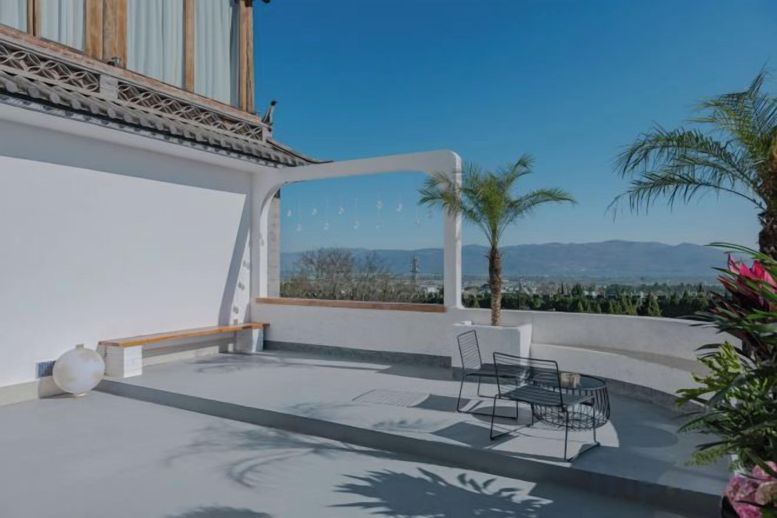 A patio with a table and chairs, a bench, and a view of the landscape.
