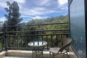 Varanda com vista para uma paisagem arborizada, duas cadeiras de vime e uma pequena mesa redonda.