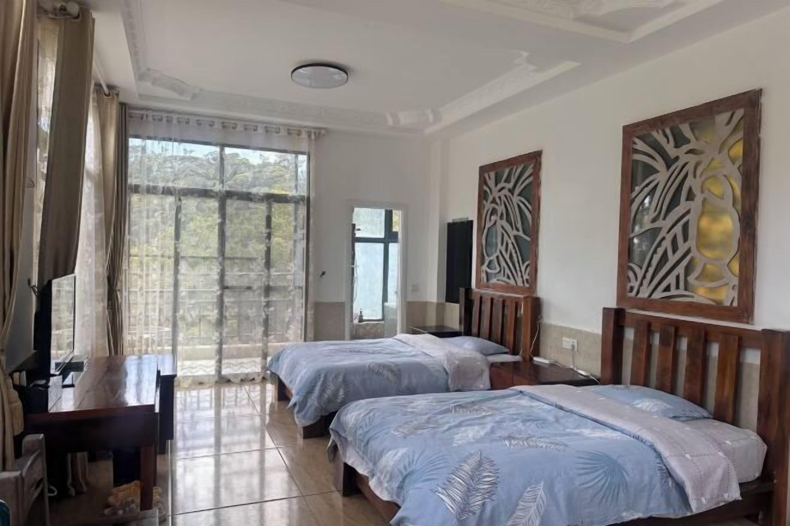 Quarto de hotel com duas camas, uma mesa de trabalho, uma televisão e uma janela grande com cortinas.