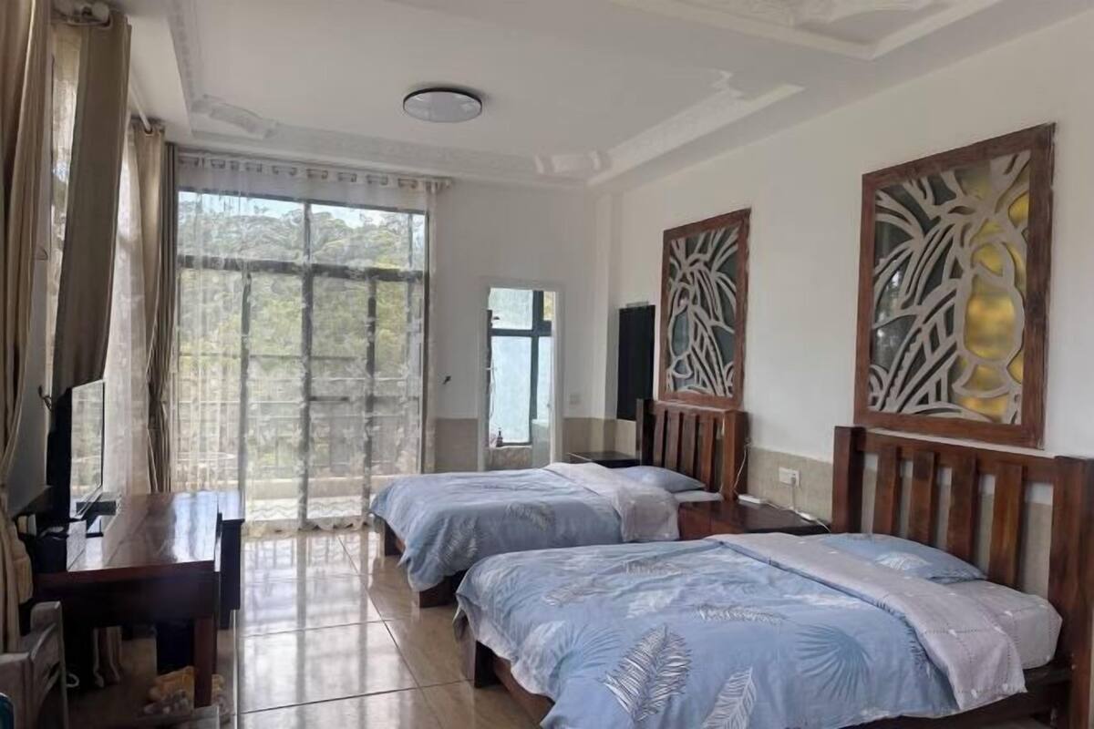 A hotel room with two beds, a desk, a TV, and a large window with curtains.