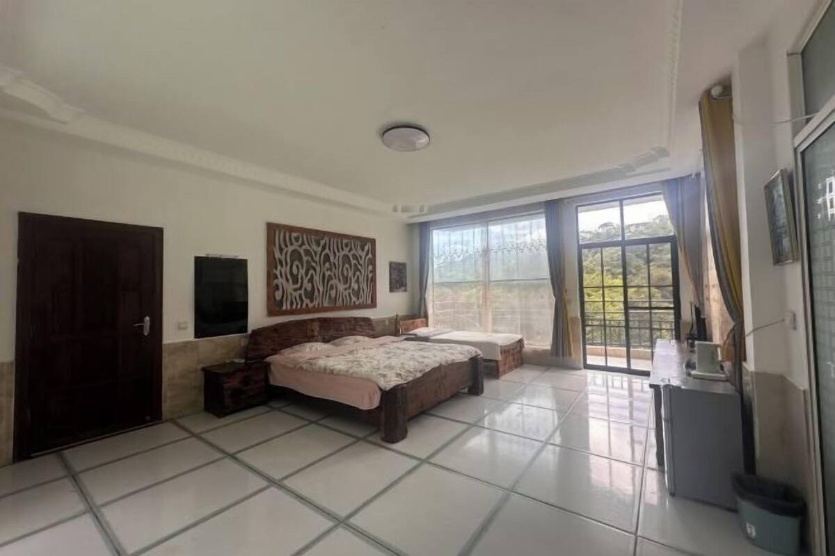 A bedroom with two beds, a desk, a TV, and a large window.
