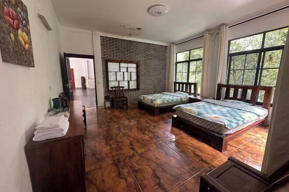 A room with a wooden floor, two beds, a desk, and a window with curtains.