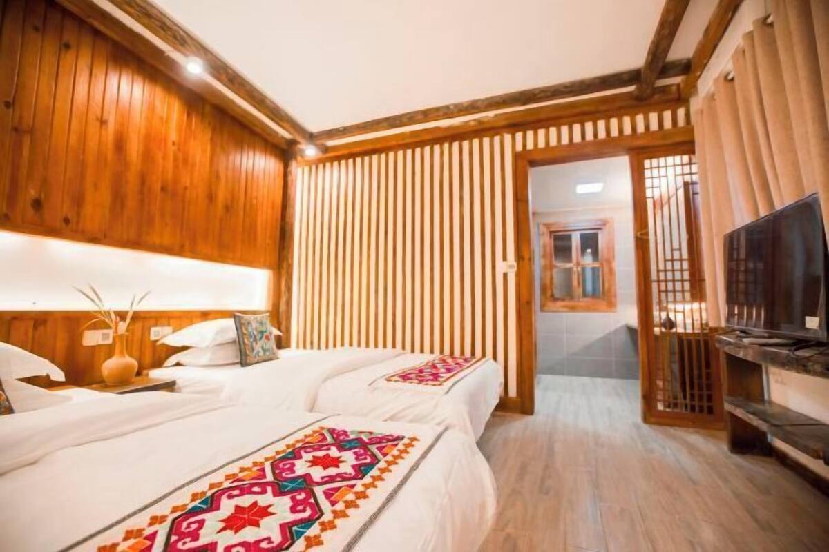Hotellihuone, jossa on puupanelointi, värikäs peitto sängyllä, televisio ja puinen kaappi.
