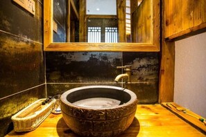 A rustic bathroom with a large, round, stone sink, wooden walls, and a mirror above the sink.
