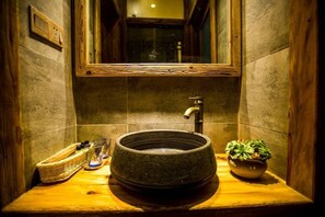 A bathroom with a round basin, a mirror, a window, and a potted plant.