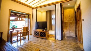 A room with a wooden floor, a television on a wooden stand, a dining table with chairs, and a sliding door leading to another room. - Sansheng Garden Inn (Puzhehei Xianrendong Shop) (Qiubei)