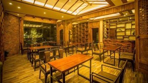 A restaurant with wooden tables and chairs, a high ceiling with skylights, and a stone wall. - Sansheng Garden Inn (Puzhehei Xianrendong Shop) (Qiubei)