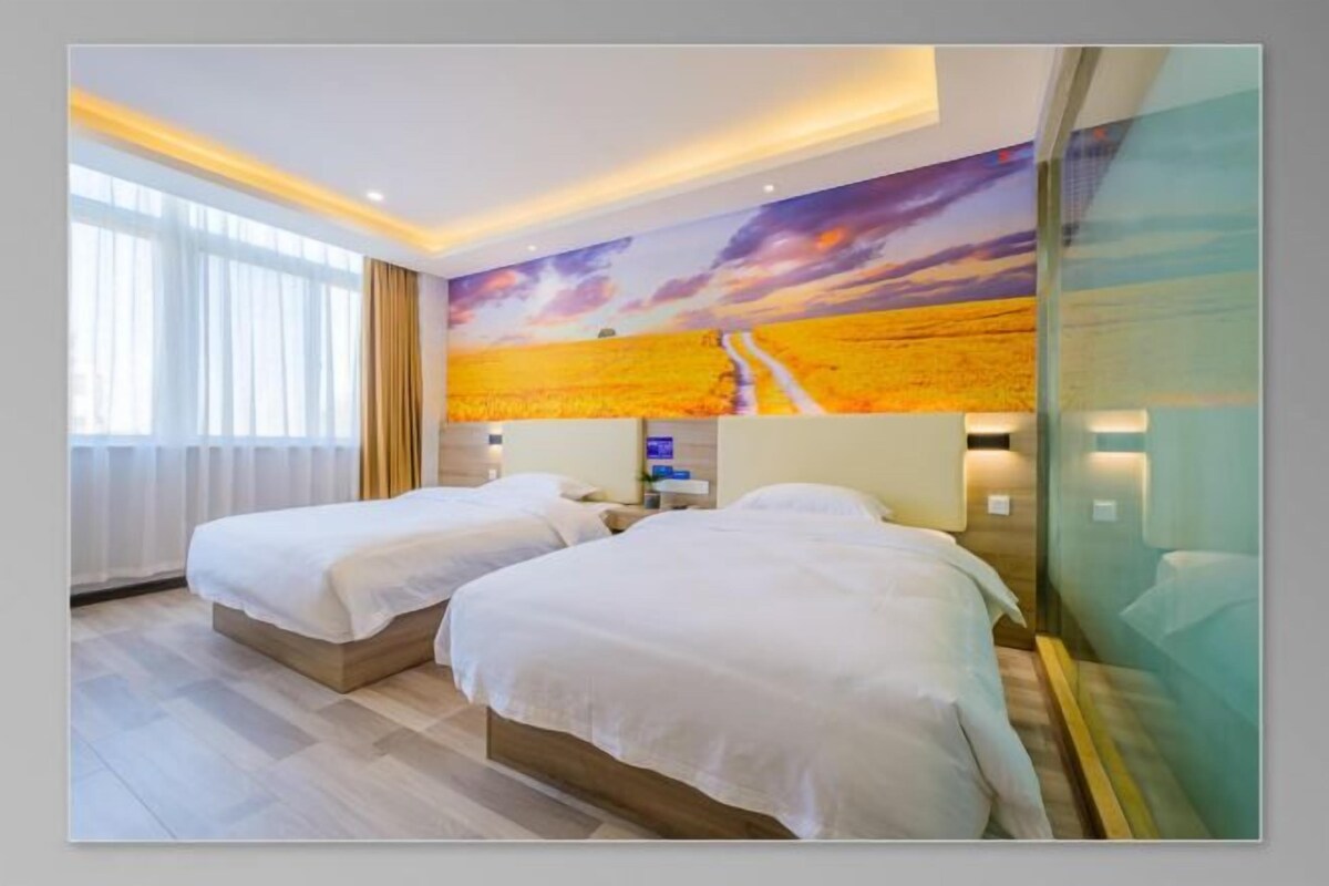 A hotel room with two beds, a large window, and a sunset mural on the wall.