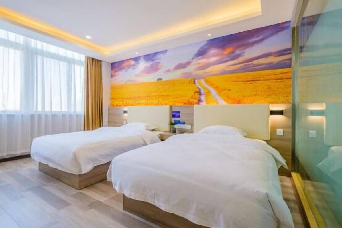 A hotel room with two beds, a large window with curtains, a wall mural, and a bedside table.