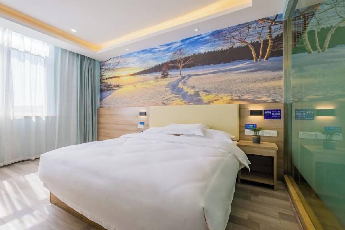 A hotel room with a large bed, a nightstand, a wall-mounted TV, and a window with curtains.