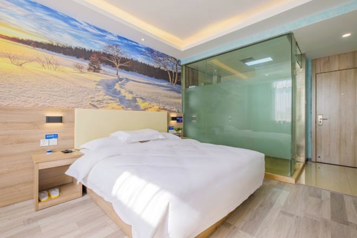 A hotel room with a bed, a nightstand, a glass partition, and a mural on the wall.