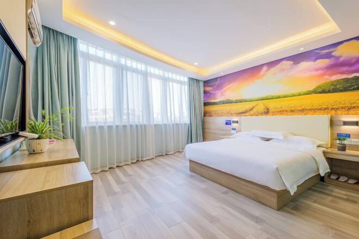 A hotel room with a large bed, a desk, and a view of a sunset mural.