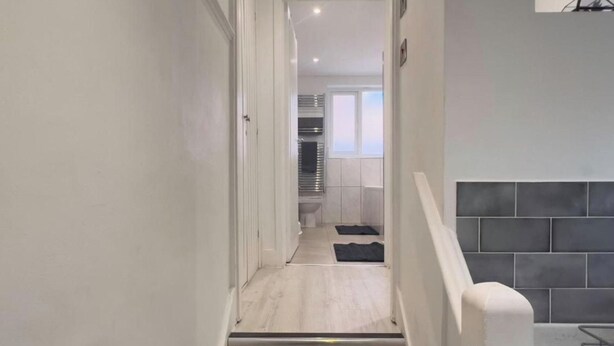 Ein schmaler Flur führt zu einem Badezimmer mit Toilette, Waschbecken und Fenster.