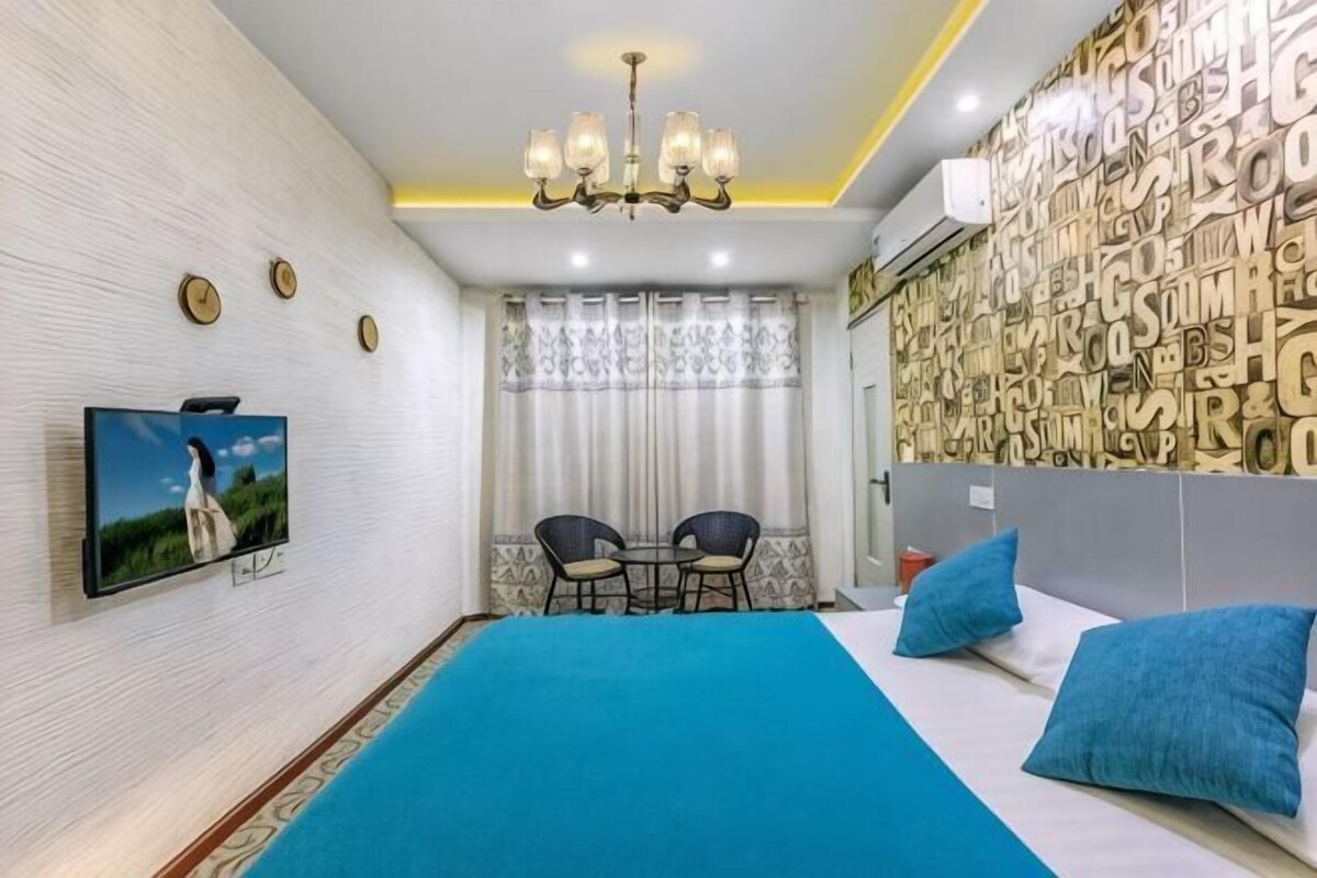 A bedroom with a bed, a TV, a chandelier, a wall clock, and a window with curtains.